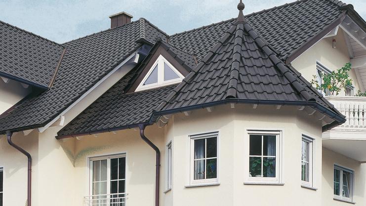 Stilvolles, helles Wohnhaus mit mehreren Erkern, Balkon und umgebenden Gartenpflanzen.