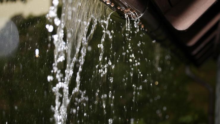 Wassertropfen fließen aus einem Regenblech herab, mit verschwommenem Hintergrund und sanfter Lichtreflexion.