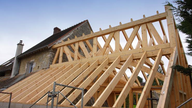 Holzgerüst eines Daches im Bau über einem alten steinernen Gebäude, mit einer Treppe und Holzlatten sichtbar.