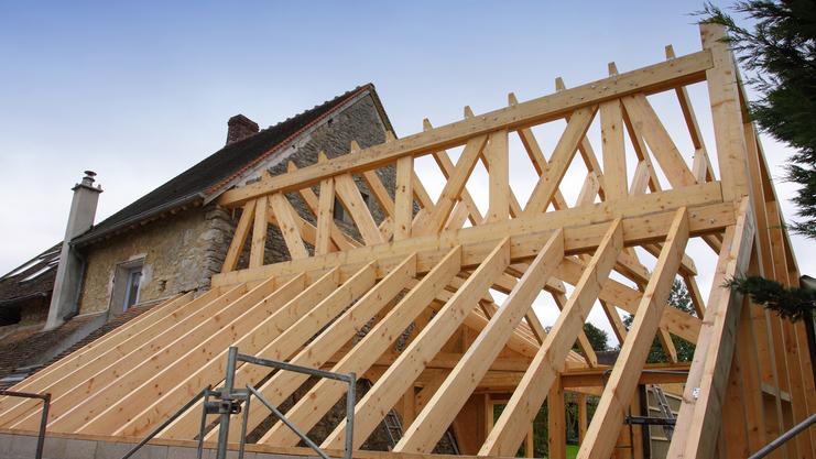 Holzgerüst eines Daches im Bau über einem alten steinernen Gebäude, mit einer Treppe und Holzlatten sichtbar.